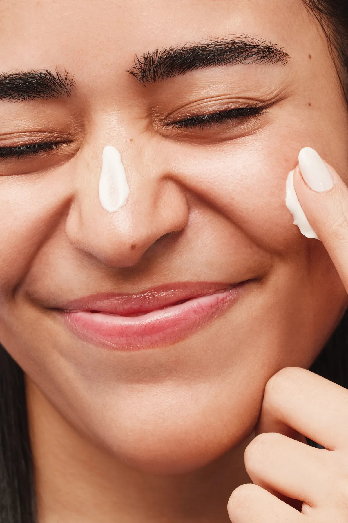 Smiling model applying cream to her cheeks for the Sephora Skincare Savvy campaign
